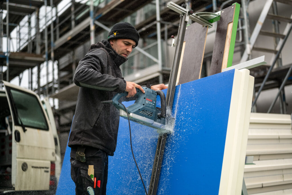 Holzbau Arbeiter sägt blaue Platte im Freien.